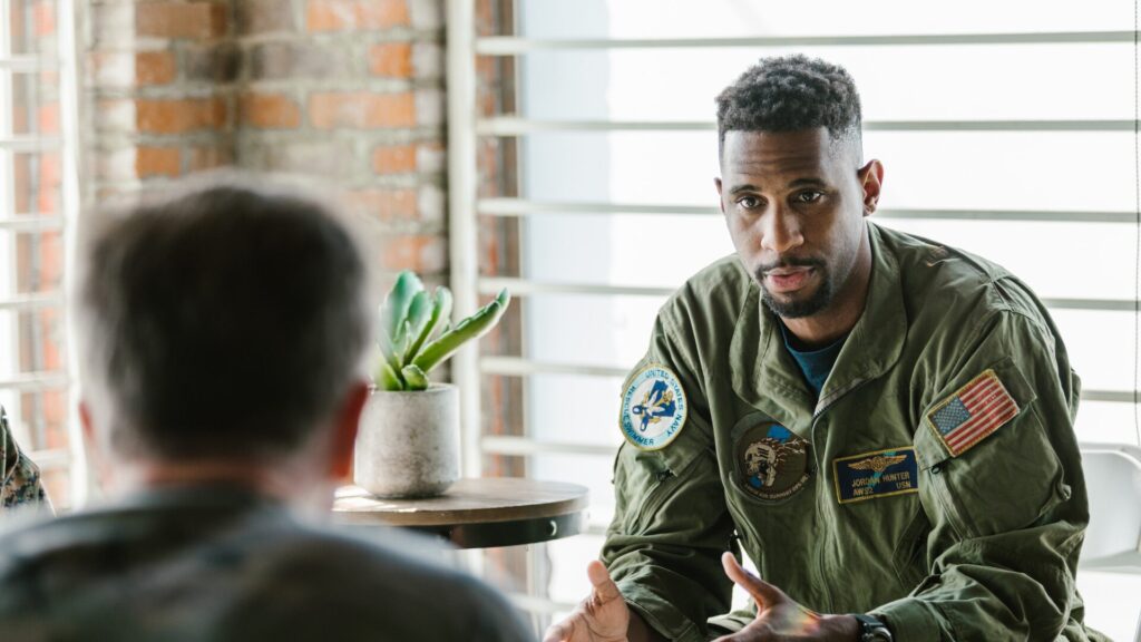 A veteran in military apparel sitting with a licensed therapist, working through trauma in a supportive environment.