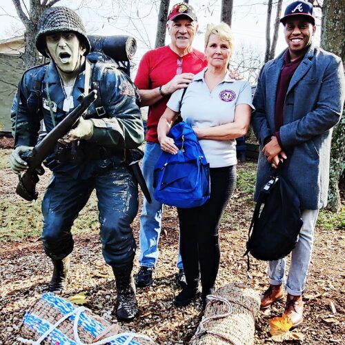 Joe and Carol from AboutFace-USA® presenting a grocery bag mat to a homeless veteran, symbolizing their commitment to breaking barriers and providing support.